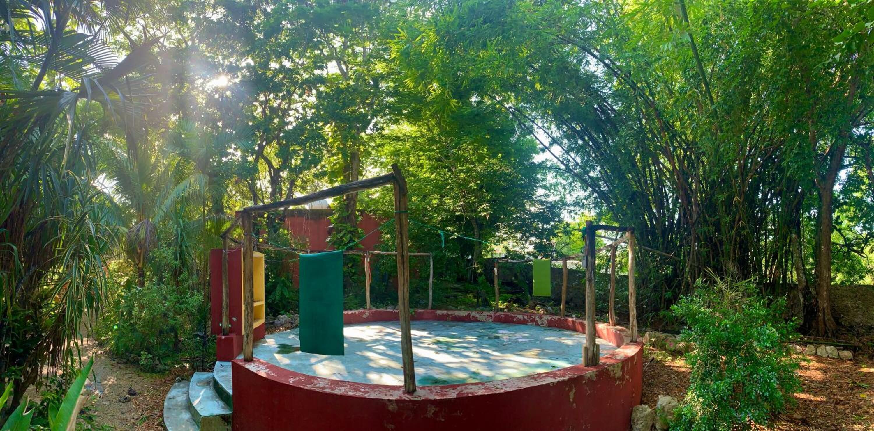 A circular outdoor area with a red border, surrounded by dense greenery and trees.