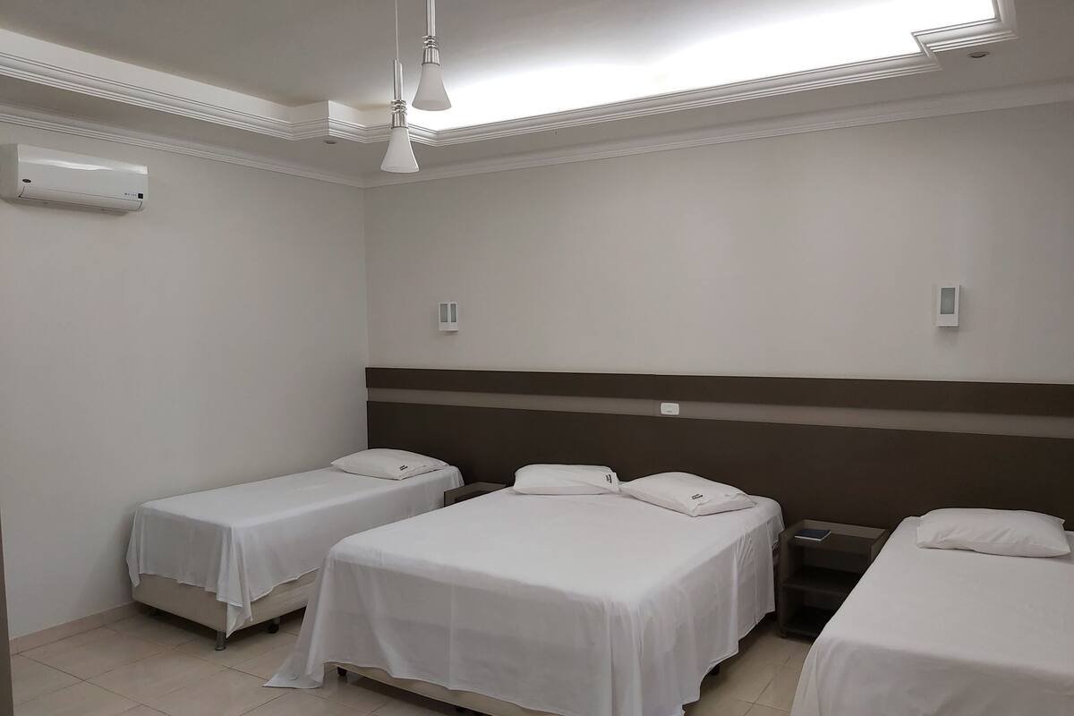 Ein Hotelzimmer mit drei Einzelbetten, einem Deckenventilator und einem Fenster mit Blick.