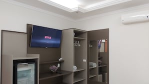 A modern room with a built-in TV displaying 'NETFLIX', a mini-fridge, and a wardrobe with shelves and hanging space. - Pousada DuKalango (Caldas Novas)