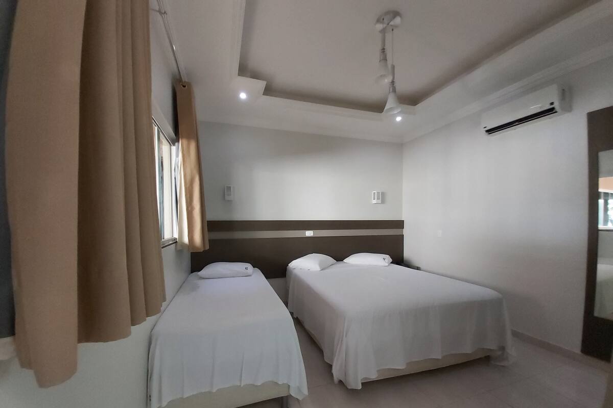 Ein Hotelzimmer mit zwei Einzelbetten, einem Deckenventilator, einer Klimaanlage und einem Fenster mit Vorhängen.