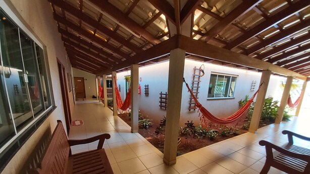 A covered outdoor area with wooden benches, a tiled floor, and a hammock. - Pousada DuKalango (Caldas Novas)