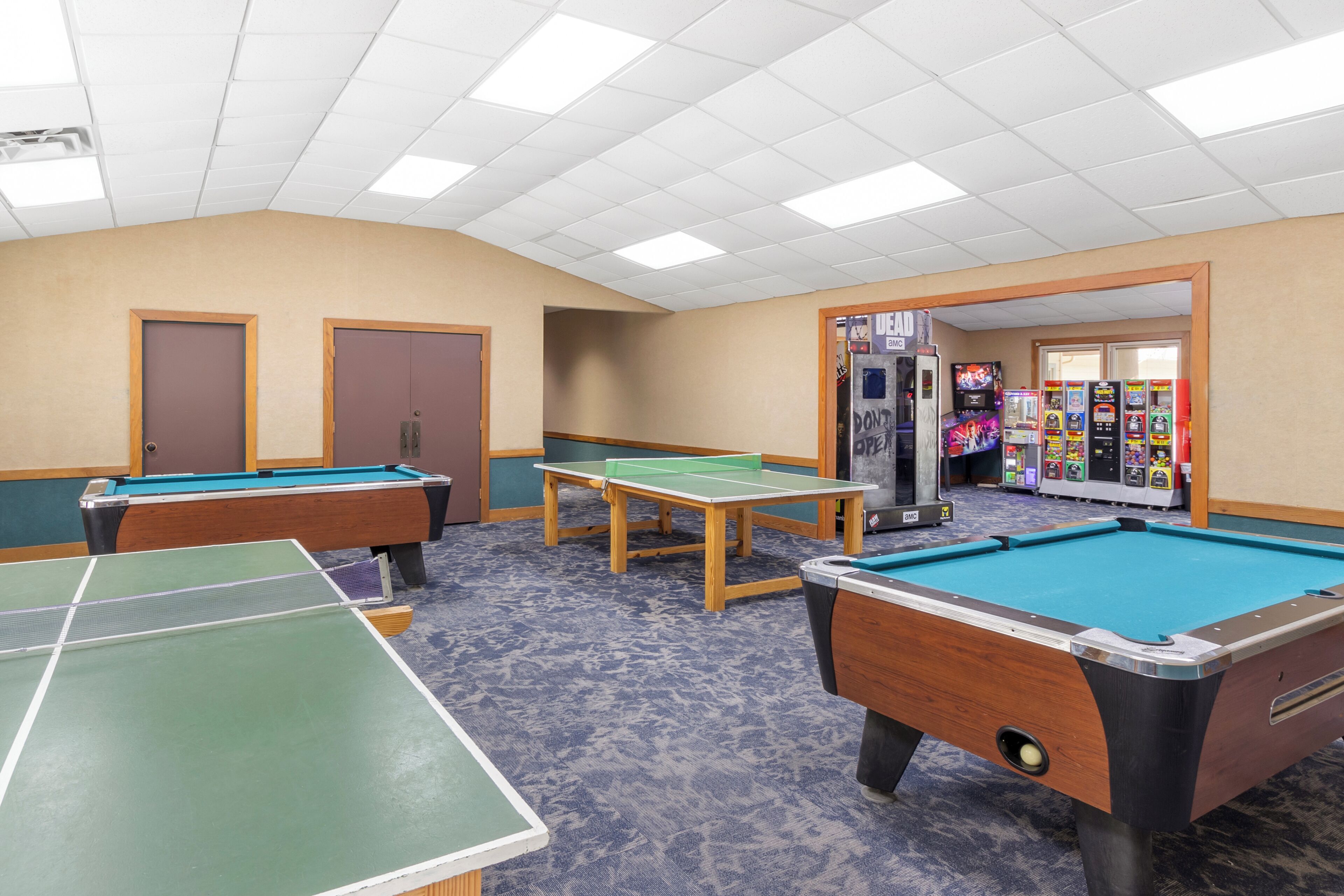 A pool table area with multiple tables, a door, and a vending machine in the background.
