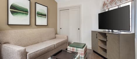 A living room with a beige sofa, a coffee table, a TV on a wooden cabinet, and two framed pictures on the wall.