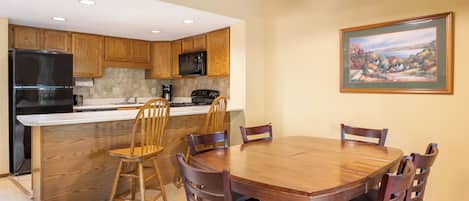 Una cocina moderna con armarios de madera, una isla central y un comedor con mesa y sillas de madera.