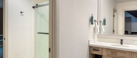 Un bagno moderno con box doccia in vetro, uno specchio grande e mobili contenitori in legno.