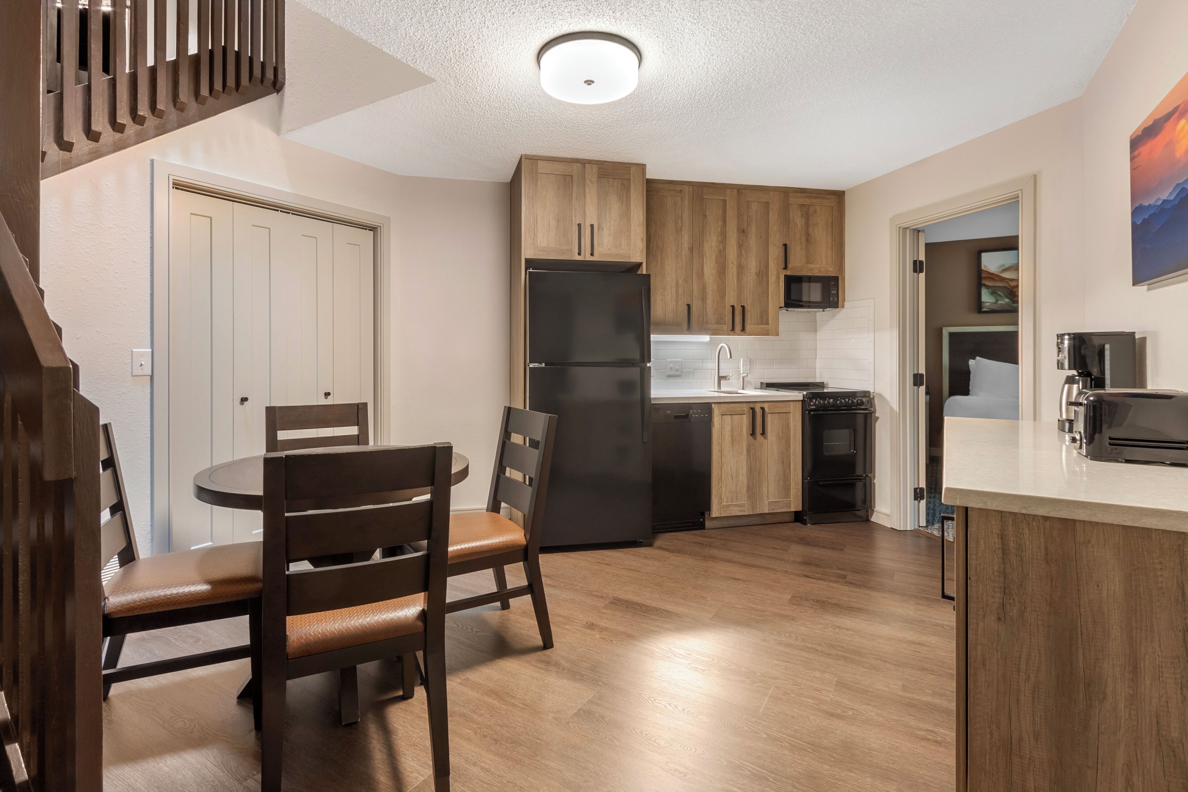 Eine moderne Küche mit Holzschränken, einem schwarzen Kühlschrank und einem Essbereich mit rundem Tisch und Stühlen.