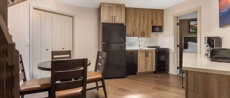Una cocina moderna con armarios de madera, un refrigerador negro y un comedor con una mesa redonda y sillas.