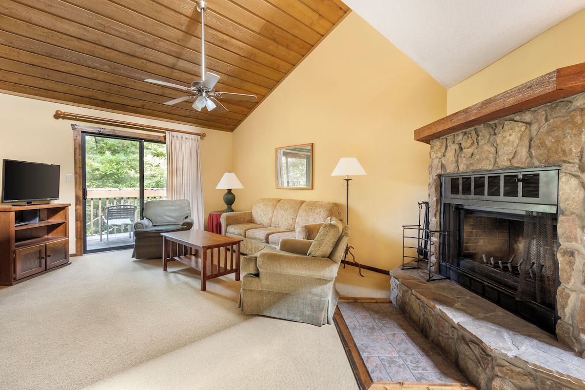 A cozy living room with a stone fireplace, a ceiling fan, a television, and a sofa.