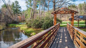 A wooden bridge leading to a gazebo in a park with a pond and trees.