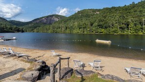 A lakeside beach with lounge chairs and a dock.