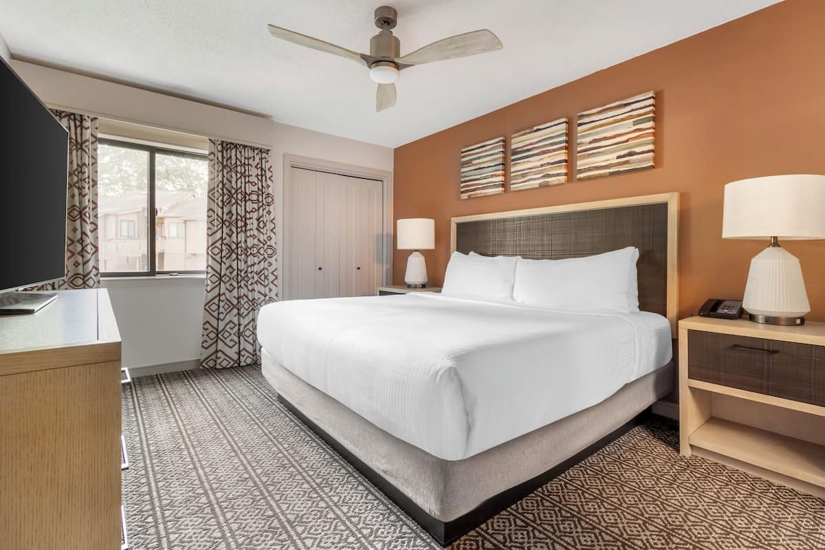 A hotel room with a large bed, a desk, a chair, a ceiling fan, and a window with curtains.