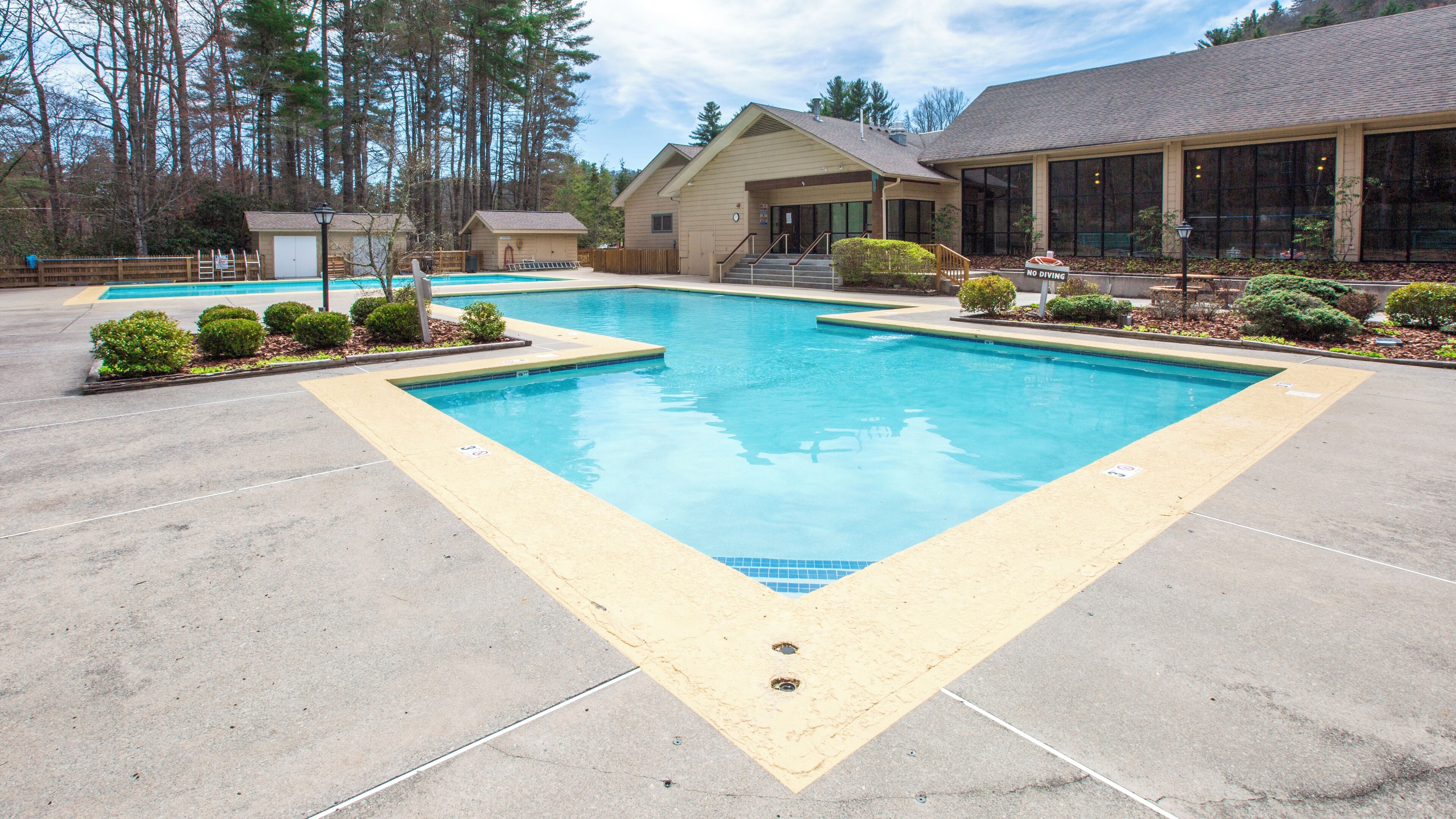 A large rectangular pool with a surrounding deck, a building with large windows, and a sign indicating no diving.