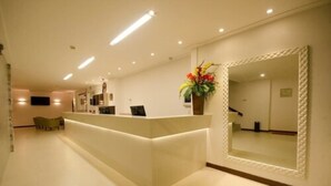 A reception area with a reception desk, a large mirror, and a vase with flowers. - Pena Branca Hotel e Eventos (Santo Antonio de Jesus)