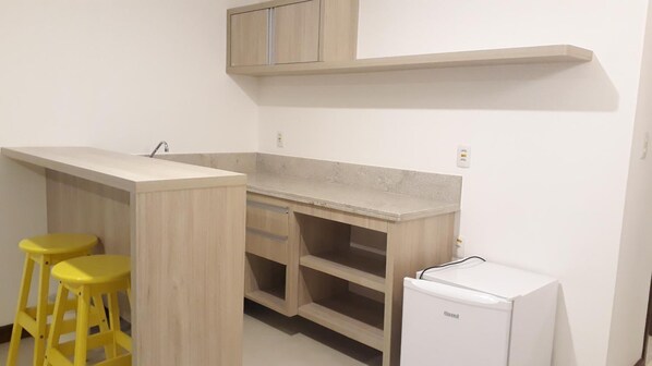 Una cocina pequeña con cubierta de madera, dos taburetes amarillos, un refrigerador blanco y un armario de madera sobre la encimera.