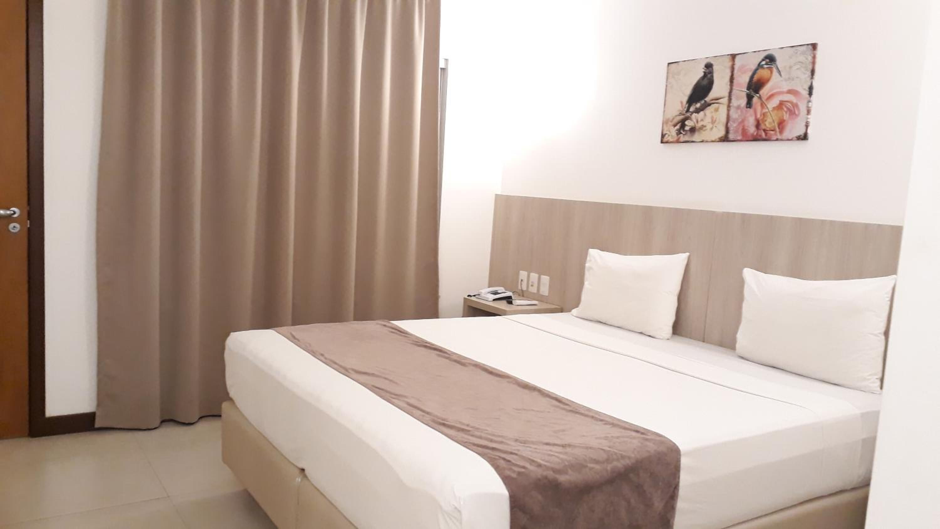 Una habitación de hotel con una cama, una mesita de noche con teléfono y un cuadro en la pared.