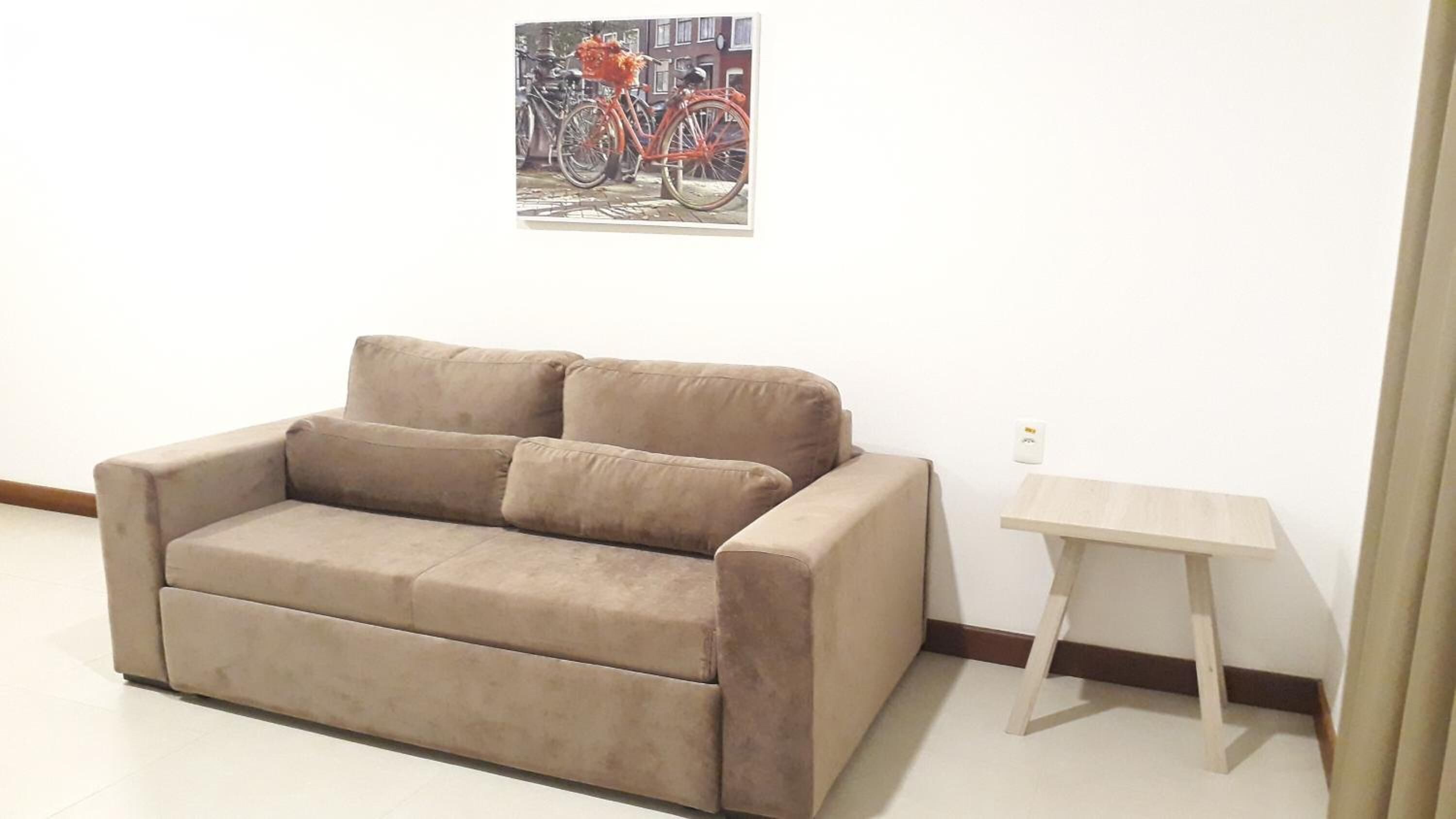 Un sofá color beige con dos cojines, una mesita de madera y un cuadro con una bicicleta en la pared.