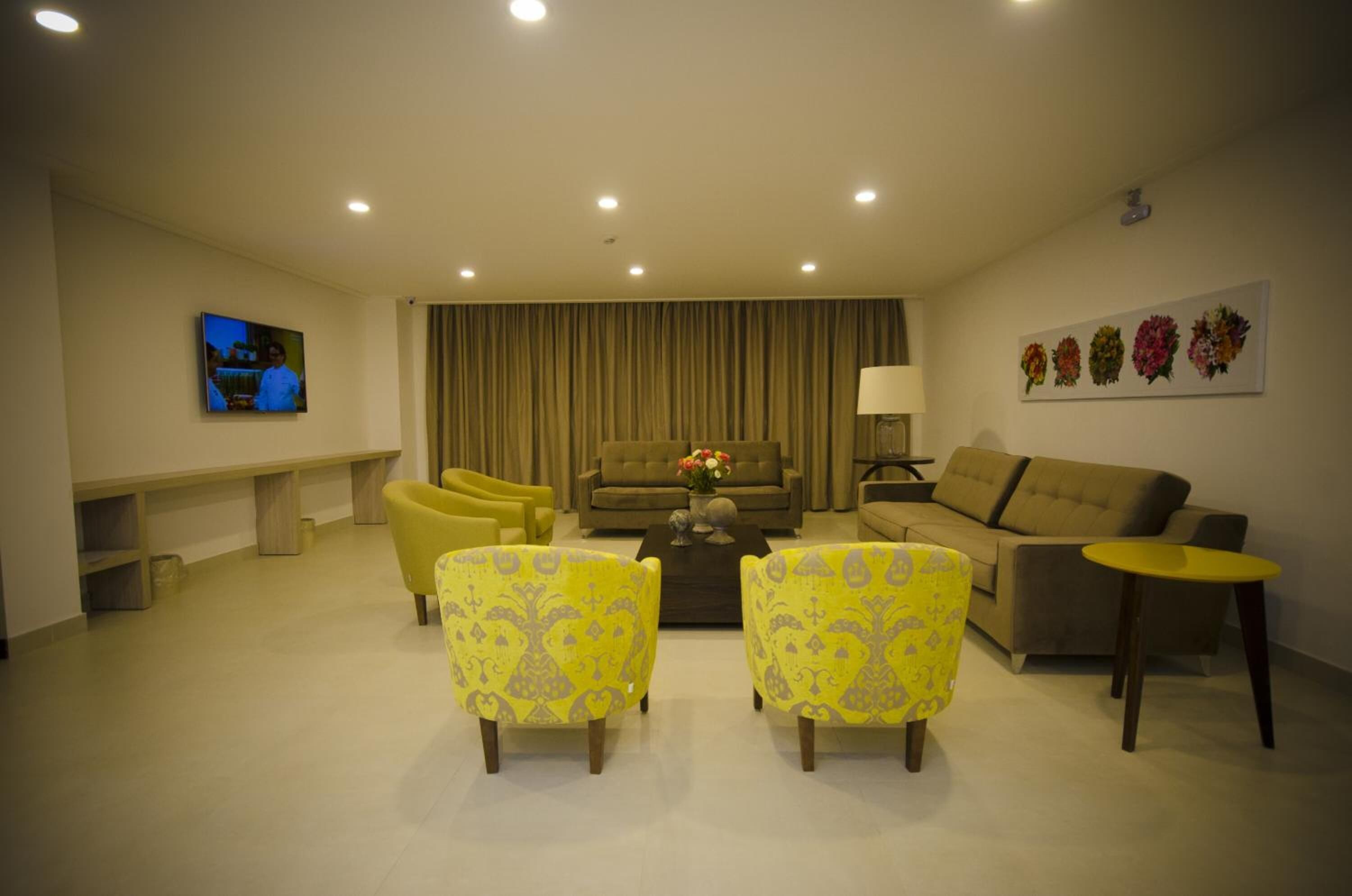 A modern living room with a sofa, two yellow armchairs, a coffee table with flowers, a TV, and a painting of flowers on the wall.