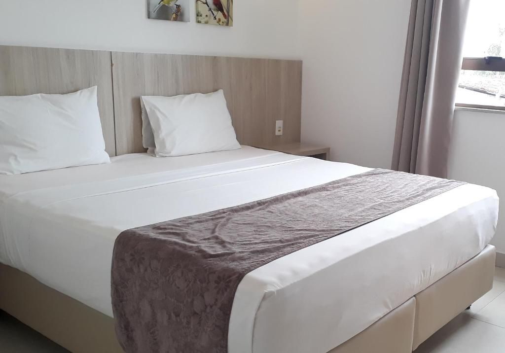 Una habitación de hotel con una cama grande, un cabecero y una ventana con cortinas.