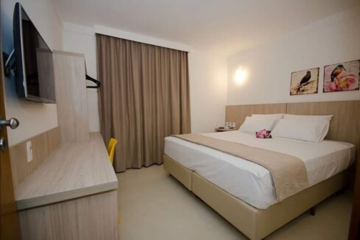 Une chambre d’hôtel avec un lit, une télévision, un bureau et une fenêtre avec des rideaux.