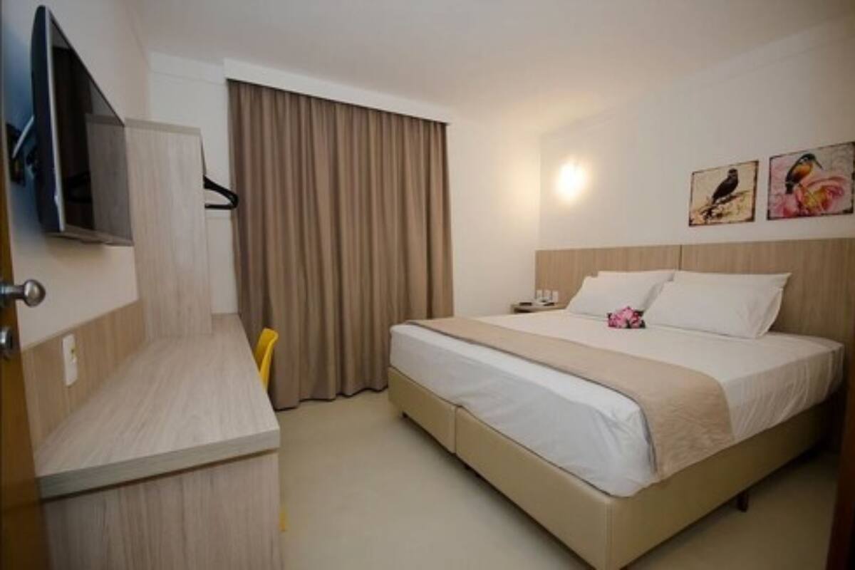 Une chambre d’hôtel avec un lit, un bureau, une télévision et une fenêtre avec des rideaux.