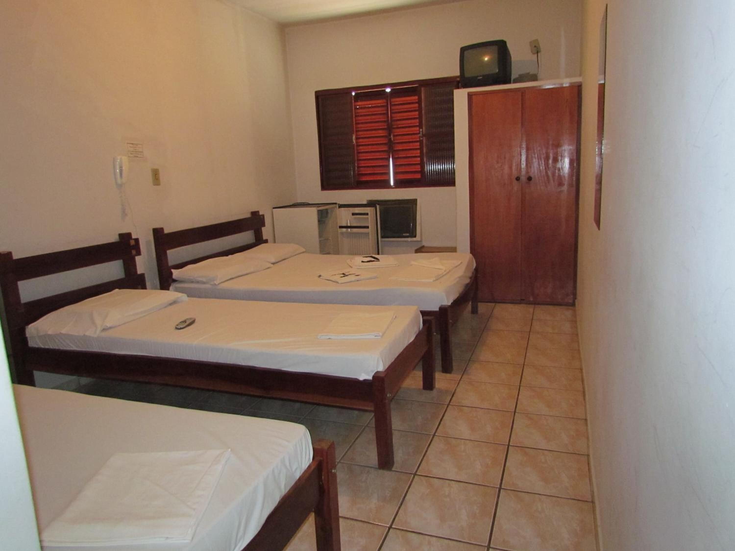 A small, compact room with three single beds, a desk with a computer, and a television on a cabinet.