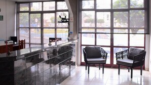 A reception area with a marble counter, two black chairs, large windows, and a view of the street. - Hotel Imperador (Caldas Novas)