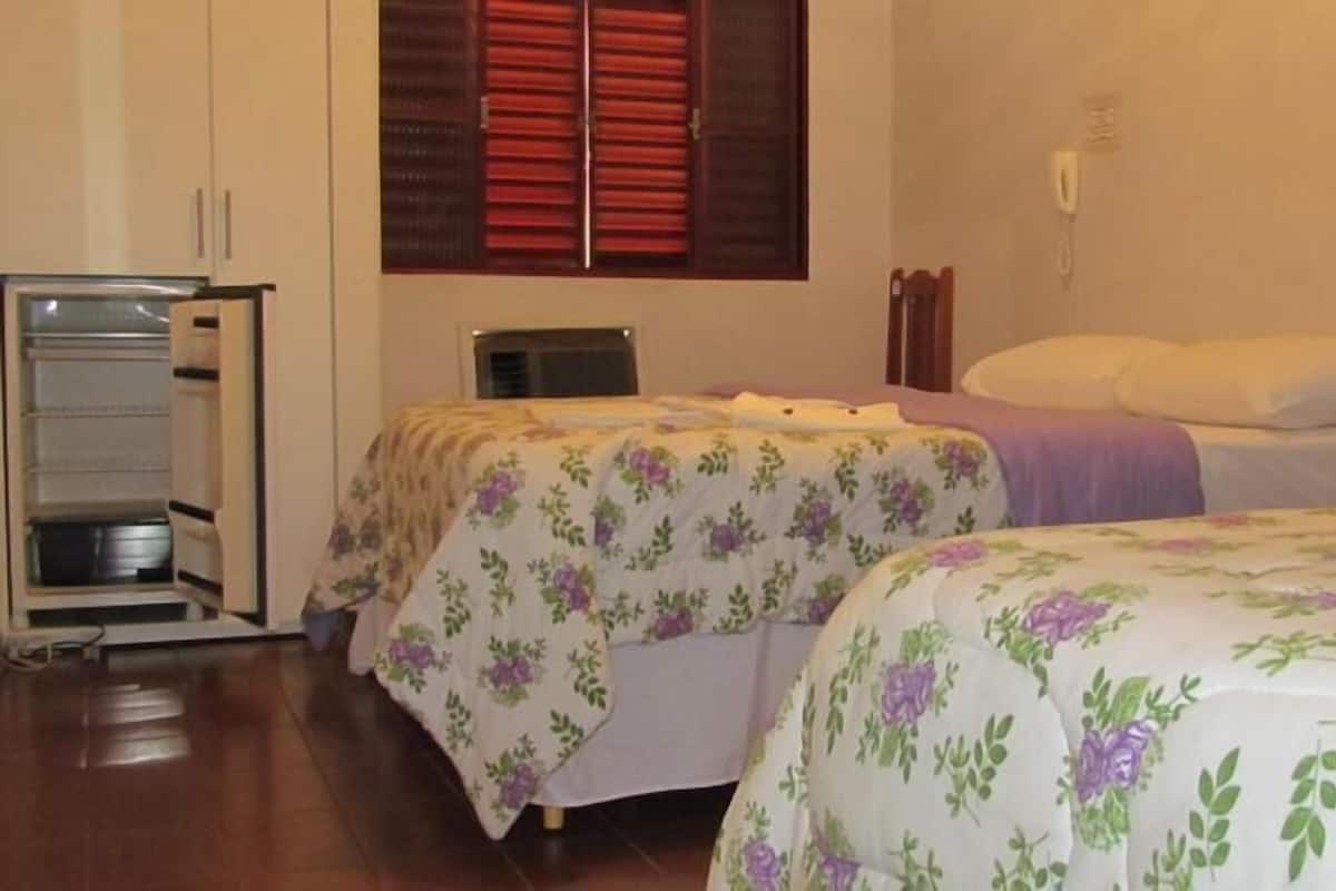 Une chambre avec deux lits, une armoire et une fenêtre avec des volets rouges.