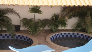Two swimming pools with blue checkered tiles, surrounded by palm trees and a tiled roof. - Hotel Imperador (Caldas Novas)
