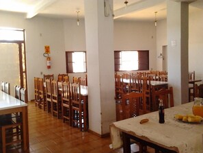 Un espace repas avec des chaises et des tables en bois, un extincteur fixé au mur et une fenêtre laissant entrer la lumière naturelle.