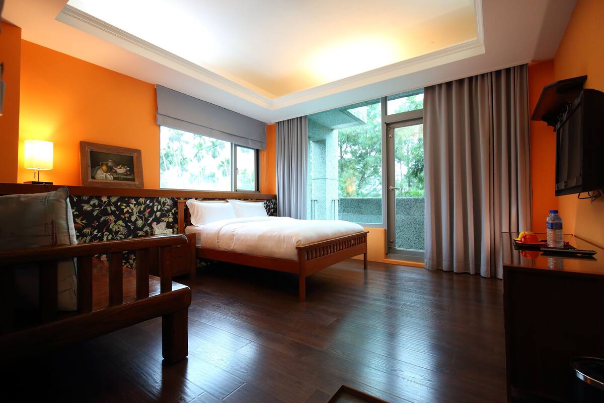 A hotel room with a bed, a desk, a chair, a TV, and a window with curtains.