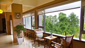 Una habitación amplia con ventanas grandes, una planta en maceta, muebles de madera y un refrigerador.