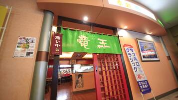 Entrada a un restaurante con toldo verde mostrando caracteres japoneses, una puerta roja y un cartel en la pared.