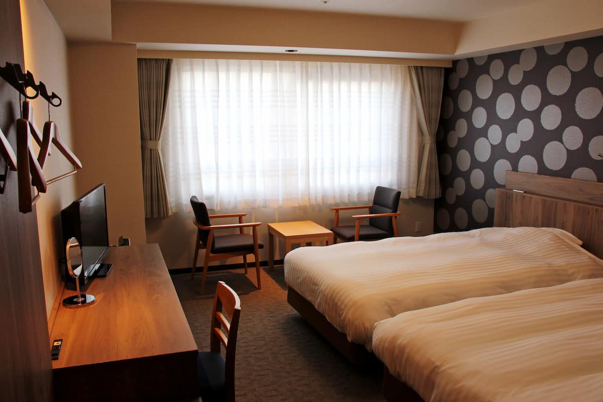 Una camera d'albergo con un letto, una scrivania con un computer, due sedie, un tavolino e una finestra con tende.