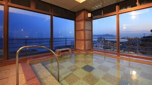 A spacious indoor area with large windows offering views of a cityscape and mountains at dusk. - Heiseikan Kaiyotei (Hakodate)