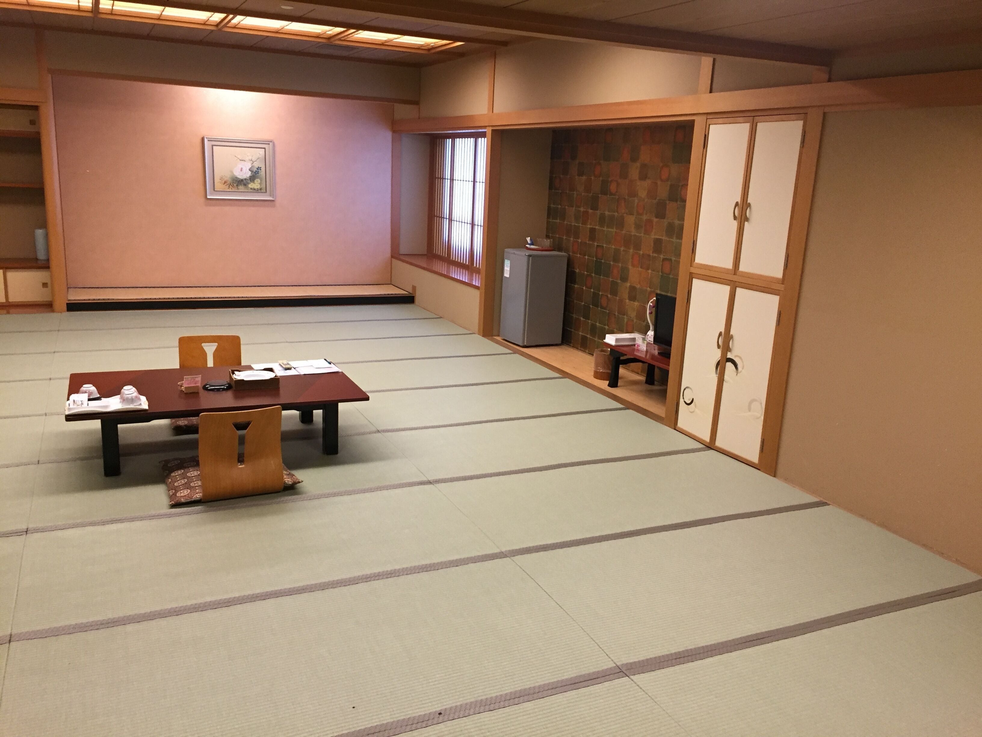 Une pièce de style traditionnel avec des tatamis, une petite table et des chaises, un réfrigérateur et des portes coulissantes.