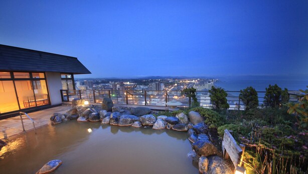 A rooftop pool with large rocks and a city view at dusk. - Heiseikan Kaiyotei (Hakodate)