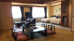 A traditional Japanese-style room with tatami flooring, a low table with cushions, a sofa, and a bed with a futon. - Heiseikan Kaiyotei (Hakodate)