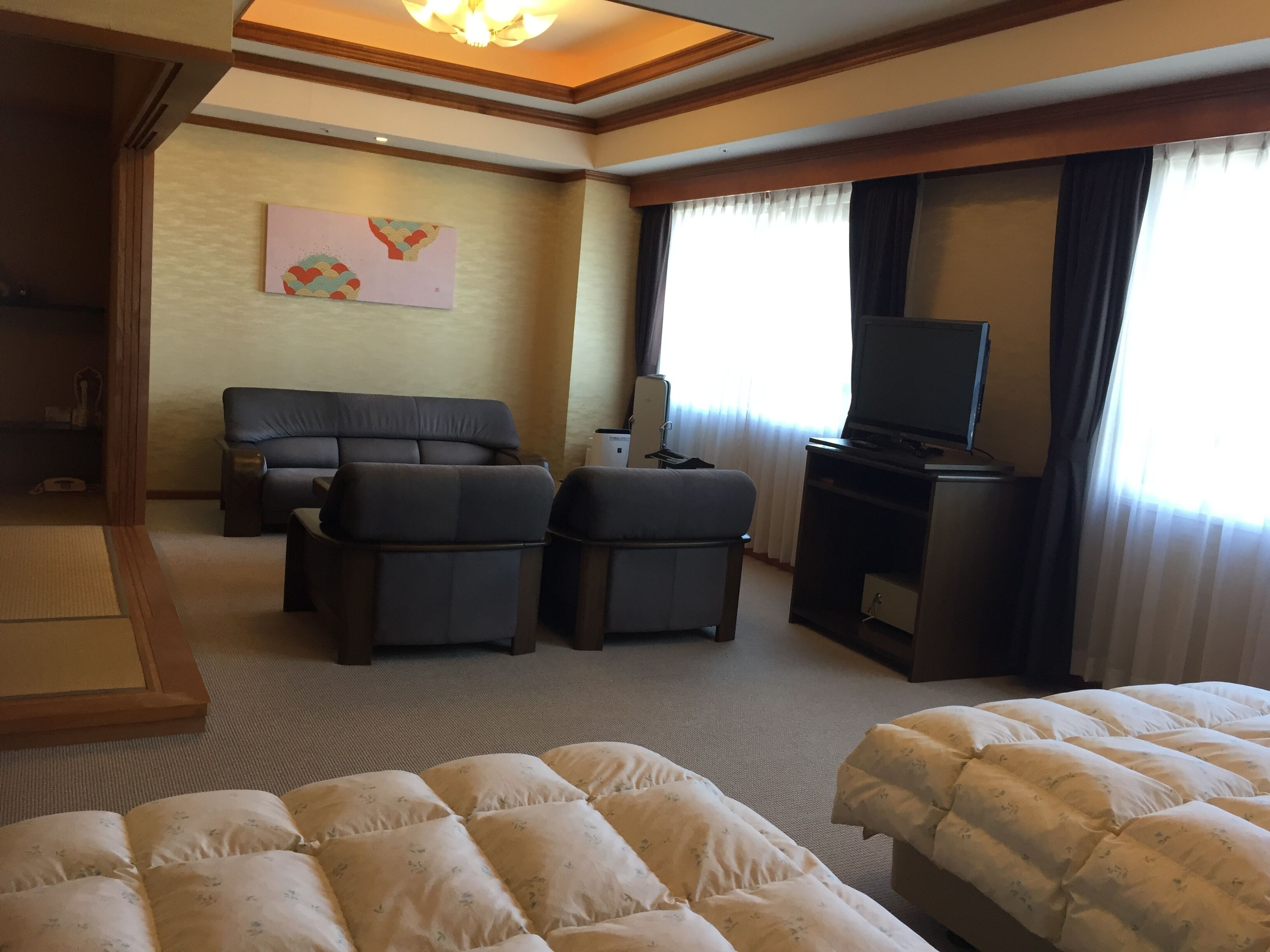 A hotel room with a sofa set, a television, a bed with a floral duvet, and a painting on the wall.