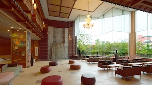 A spacious indoor area with multiple seating options, including round and rectangular tables and chairs, and a large window providing a view of greenery outside. - Heiseikan Kaiyotei (Hakodate)