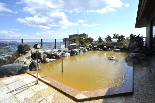Zona de aguas termales con vista al mar, rodeada de rocas y una baranda de metal.