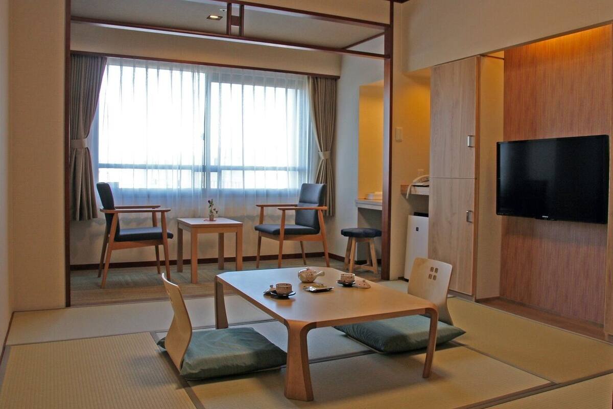 Una tradizionale stanza in stile giapponese con pavimento in tatami, un tavolino con cuscini e un televisore montato a parete.