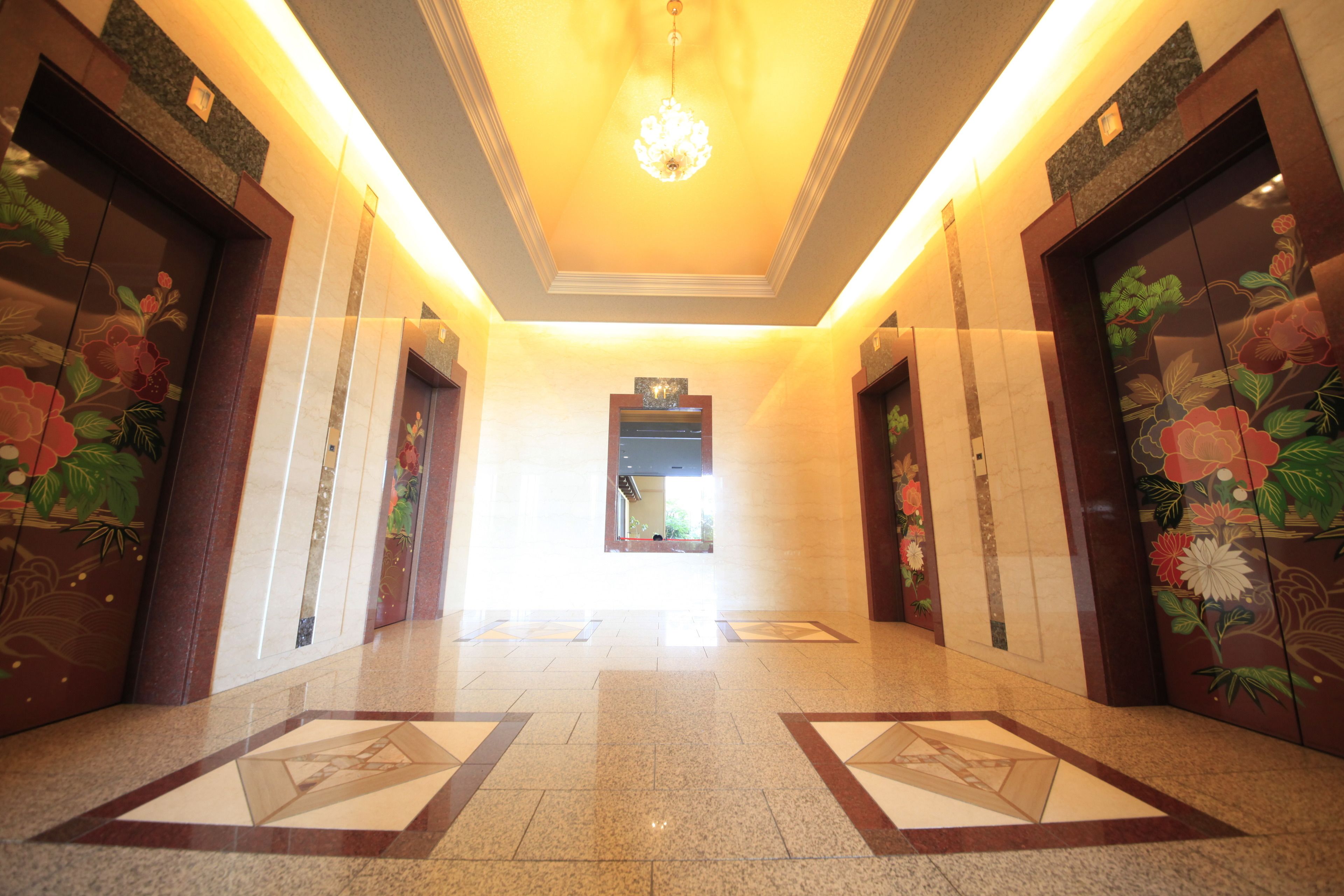A hallway with a chandelier, mirrored walls, and patterned floor tiles.