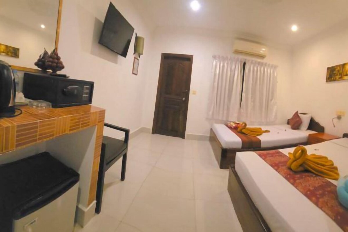 Habitación de hotel con cama, escritorio con computadora, silla, televisor en la pared y puerta.