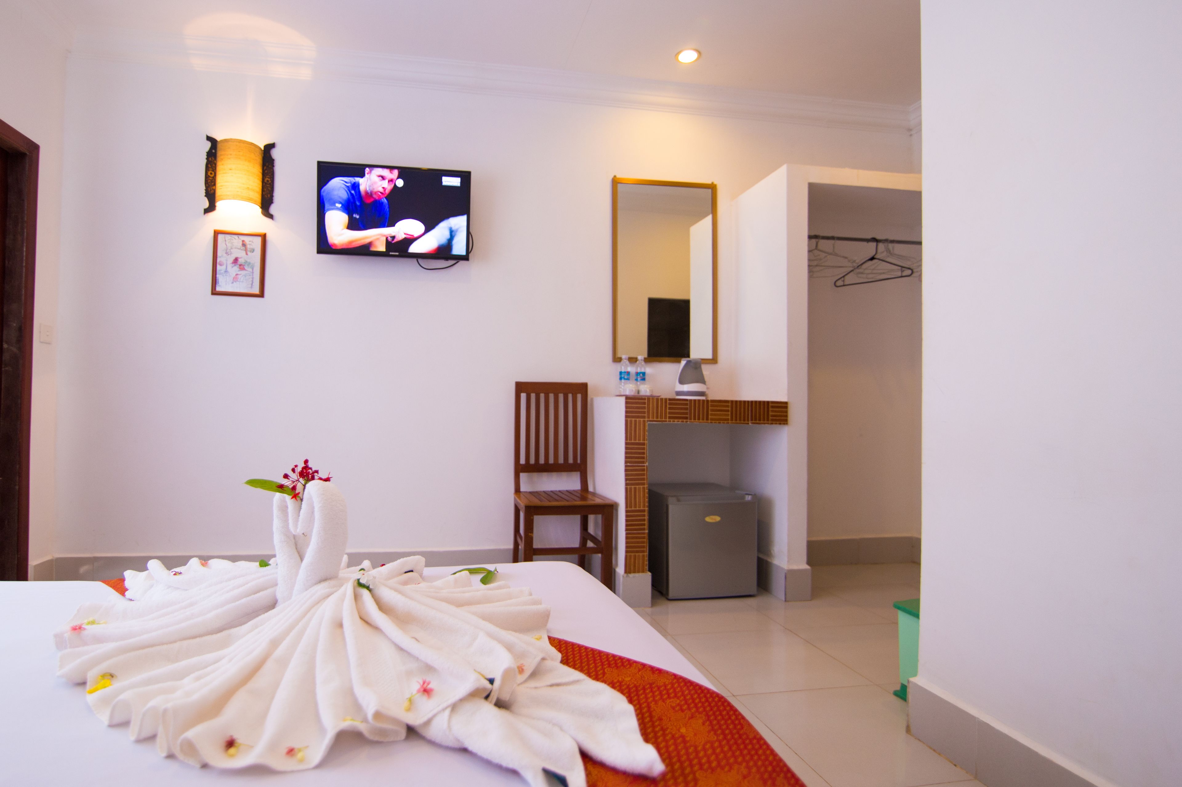 A hotel room with a bed, a television, a chair, a mirror, a refrigerator, and a laundry area.