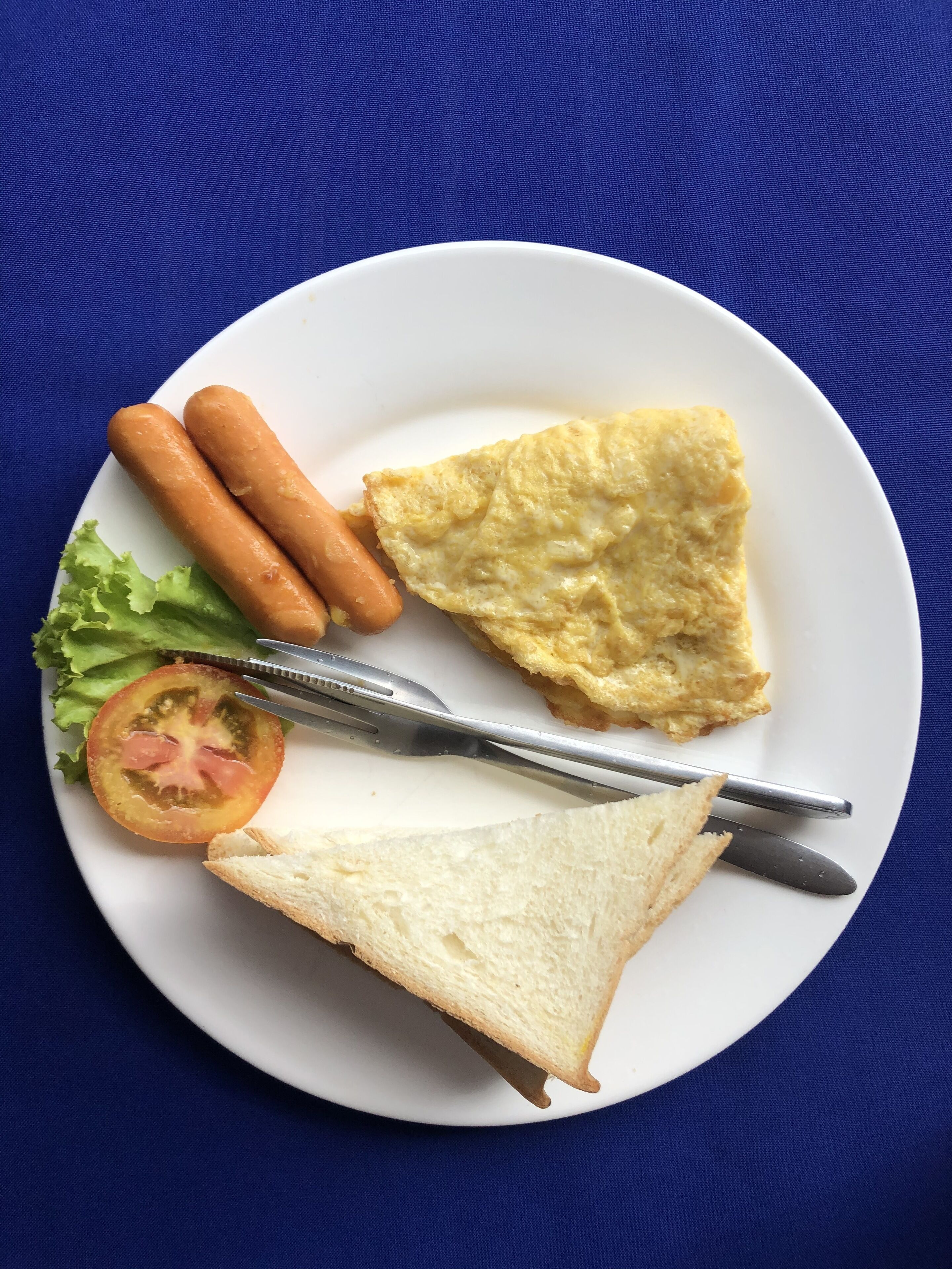 Ein Teller mit zwei Bratwürsten, einer Toastscheibe, etwas Rührei, einer Tomatenscheibe und einem kleinen Blattsalat.