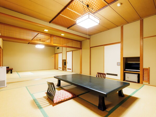 A traditional Japanese room with tatami flooring, a low table, chairs, a television, and a refrigerator. - Chikuba Shinyotei (Hakodate)