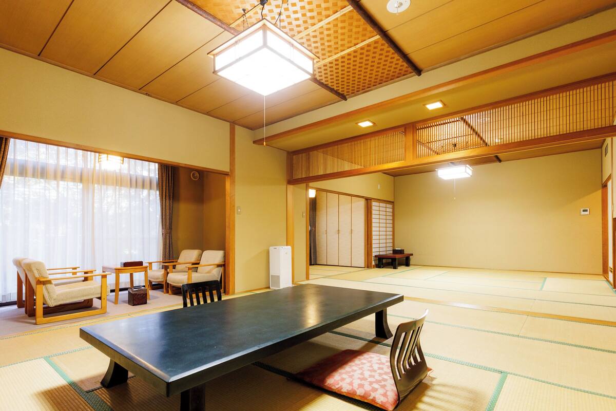 A tatami mat room with a low table, chairs, and a traditional sliding door.