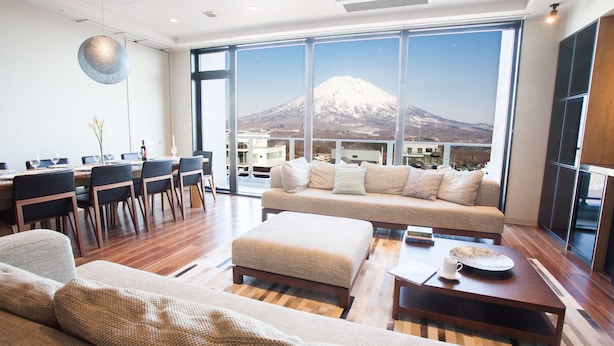 A modern living room with a large window, a sofa, a dining area, and a view of a mountain. - Hirafu 188 (Kutchan)
