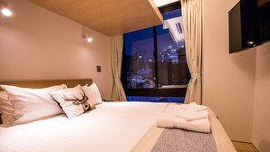 A hotel room with a large bed, a view of the city at night, and a flat-screen TV mounted on the wall. - Hirafu 188 (Kutchan)