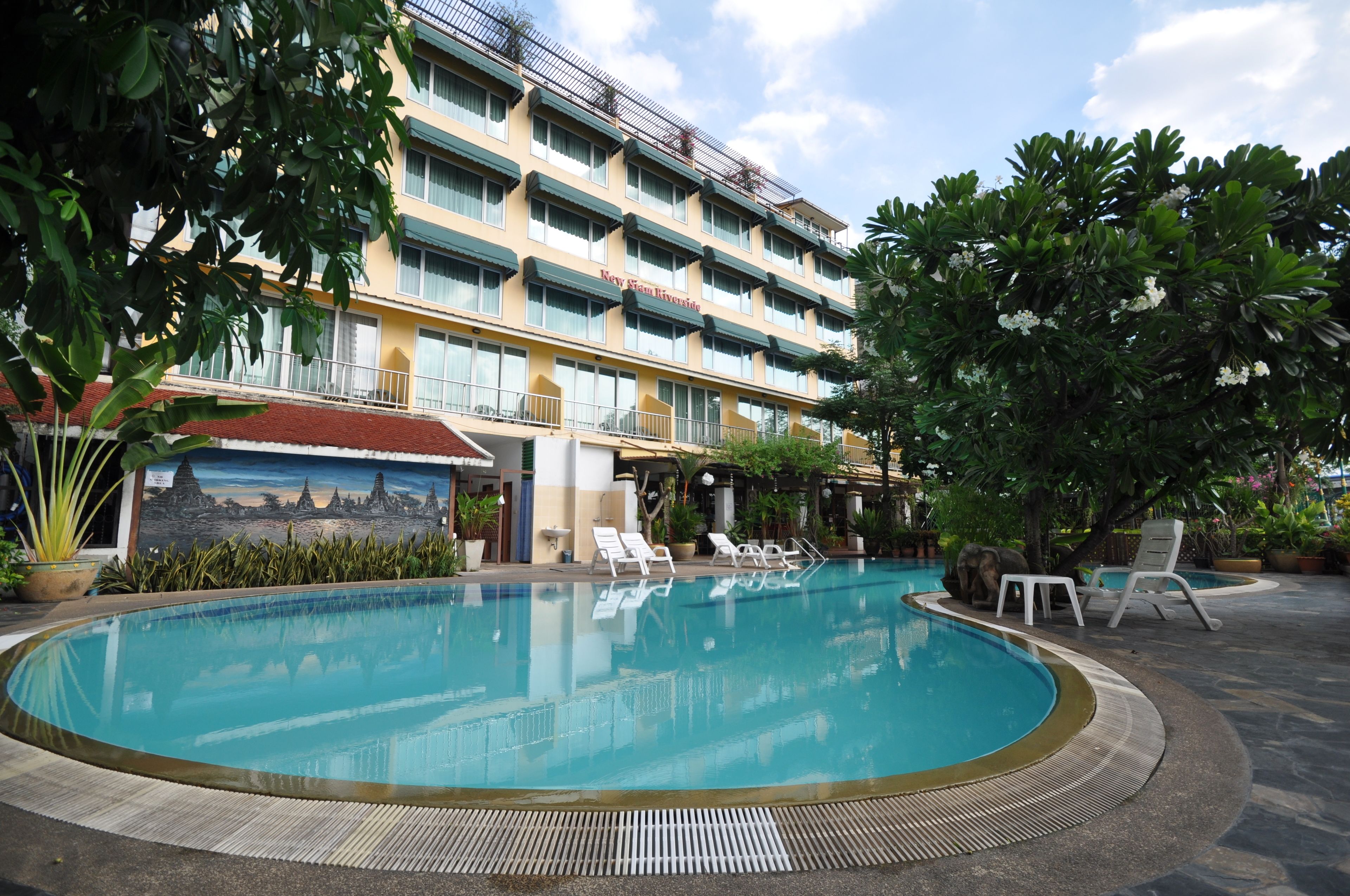 A hotel with a swimming pool, lounge chairs, and a mural.